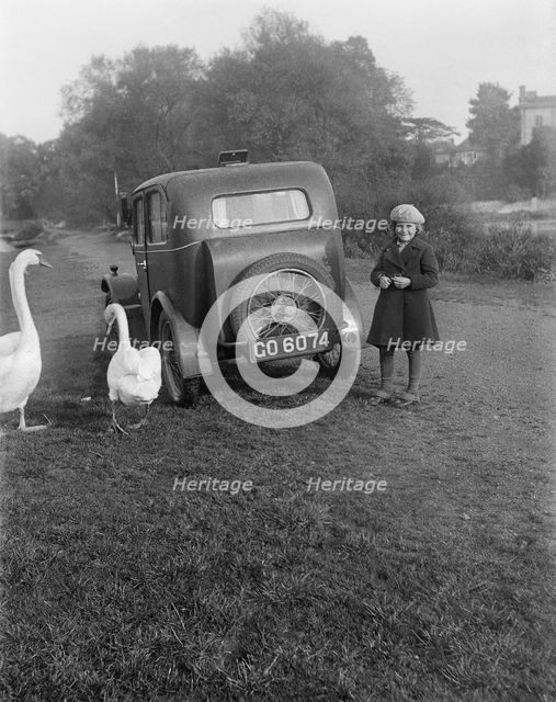 A young girl next to a motor car, probably an Austin 7, with two swans, c1930s. Artist: Unknown.