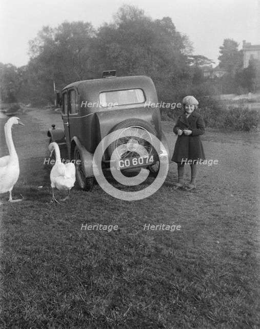 A young girl next to a motor car, probably an Austin 7, with two swans, c1930s. Artist: Unknown.