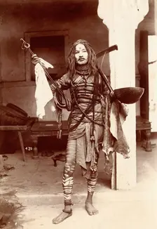 A young Indian man wearing many beads and makeup in a temple precinct, c1900. Creator: Unknown