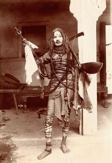 A young Indian man wearing many beads and makeup in a temple precinct, c1900. Creator: Unknown