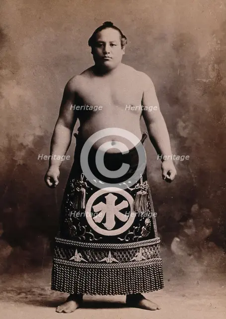 A young sumo wrestler posing in a photographic studio, wearing a richly decorated apron..., c1900. Creator: Unknown.