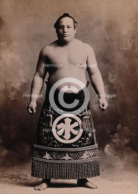 A young sumo wrestler posing in a photographic studio, wearing a richly decorated apron..., c1900. Creator: Unknown.