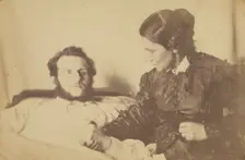 A bearded man lying in bed, his hand held by his wife who is seated next to the bed, 1870-79. Creator: Unknown