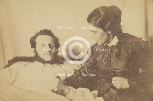 A bearded man lying in bed, his hand held by his wife who is seated next to the bed, 1870-79. Creator: Unknown.