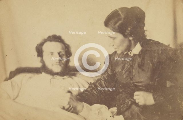 A bearded man lying in bed, his hand held by his wife who is seated next to the bed, 1870-79. Creator: Unknown.