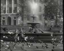 A Boy and a Girl Feeding Pigeons by One of the Fountains in Trafalgar Square with..., 1939. Creator: British Pathe Ltd