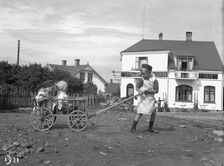 A boy pulling his brother and sister in a cart, 1911