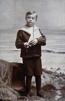 A boy with Down's syndrome, dressed in a sailor suit, standing against a nautical... Creator: Kent Coast Studio