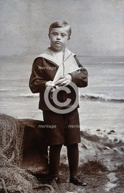 A boy with Down's syndrome, dressed in a sailor suit, standing against a nautical... Creator: Kent Coast Studio.