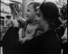 A British Woman Holding up a Young Boy Who is Waving in the Direction of a Bus as Other..., 1939. Creator: British Pathe Ltd