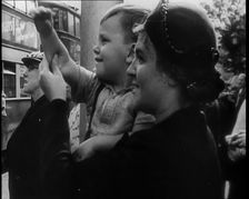 A British Woman Holding up a Young Boy Who is Waving in the Direction of a Bus as Other..., 1939. Creator: British Pathe Ltd