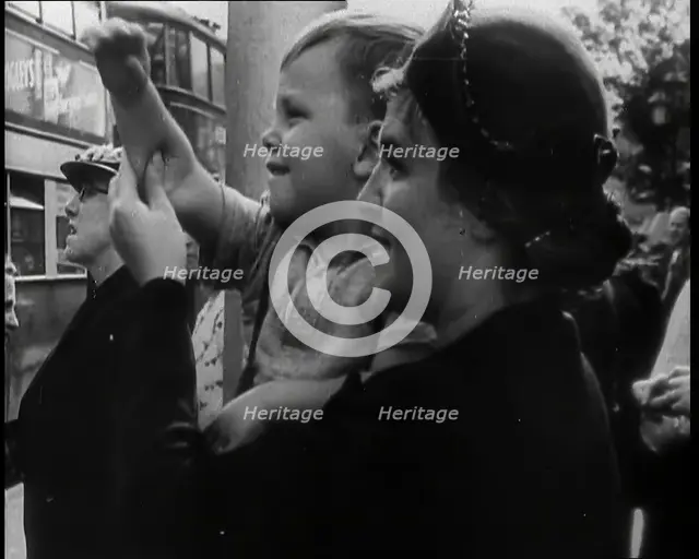 A British Woman Holding up a Young Boy Who is Waving in the Direction of a Bus as Other..., 1939. Creator: British Pathe Ltd.