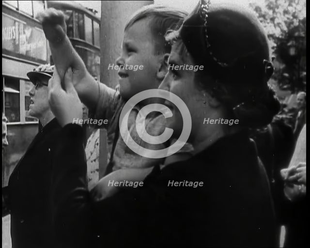 A British Woman Holding up a Young Boy Who is Waving in the Direction of a Bus as Other..., 1939. Creator: British Pathe Ltd.
