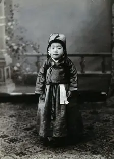 A child posing in front of a painted backdrop in a photographic studio, c1900. Creator: Unknown