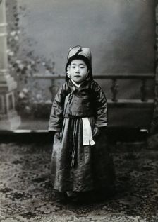 A child posing in front of a painted backdrop in a photographic studio, c1900. Creator: Unknown