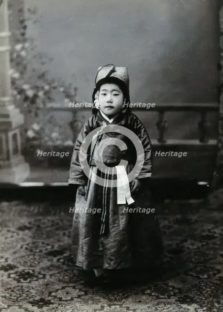 A child posing in front of a painted backdrop in a photographic studio, c1900. Creator: Unknown.