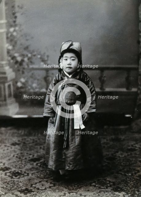 A child posing in front of a painted backdrop in a photographic studio, c1900. Creator: Unknown.
