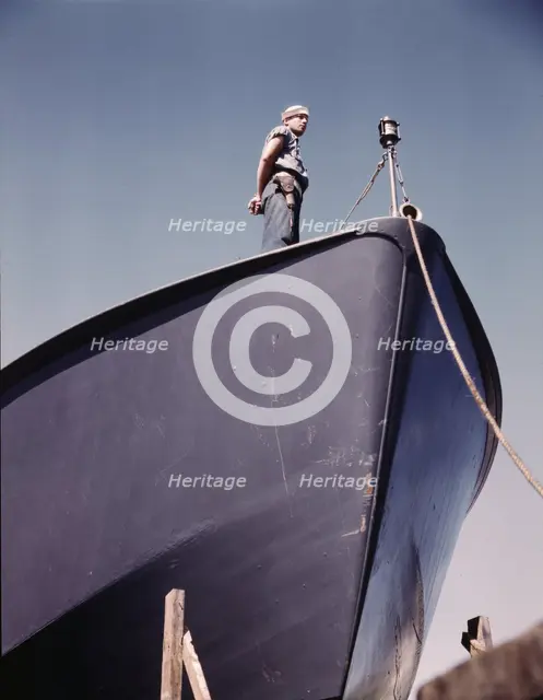 A Coast Guard sentry stands watch over a new torpedo boat under construction at a southern..., 1942. Creator: Howard Hollem.