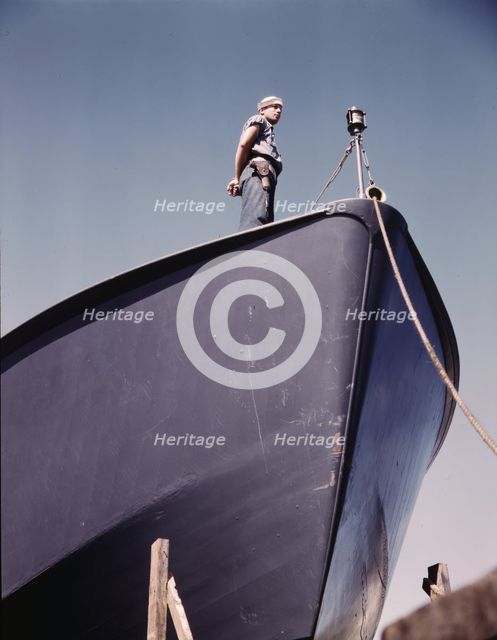 A Coast Guard sentry stands watch over a new torpedo boat under construction at a southern..., 1942. Creator: Howard Hollem.