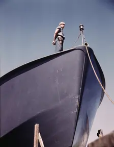 A Coast Guard sentry stands watch over a new torpedo boat under construction at a southern..., 1942. Creator: Howard Hollem