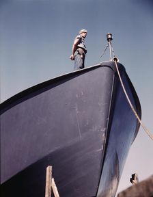 A Coast Guard sentry stands watch over a new torpedo boat under construction at a southern..., 1942. Creator: Howard Hollem