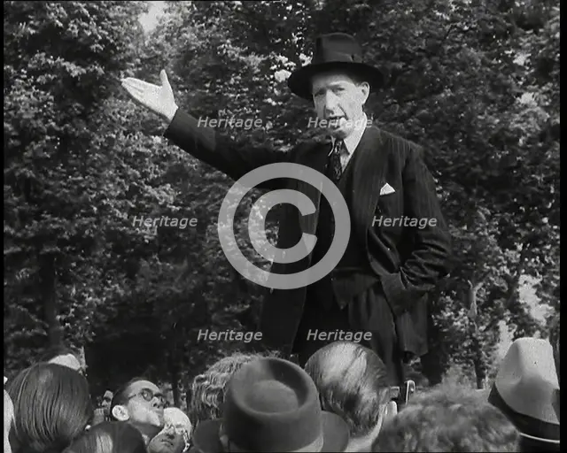 A Close up of a British Man in Dark Suit and Hat Declaiming Before a Crowd from a Raised..., 1938. Creator: British Pathe Ltd.