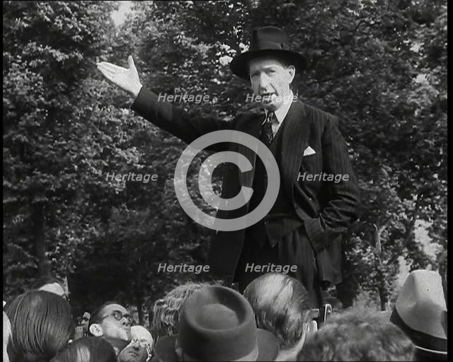 A Close up of a British Man in Dark Suit and Hat Declaiming Before a Crowd from a Raised..., 1938. Creator: British Pathe Ltd.