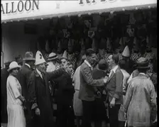 A Crowd of People Standing in Front of a Carnival Game. A Man in a Clown's Hat Encourages..., 1924. Creator: British Pathe Ltd