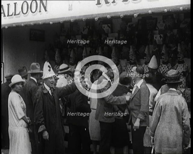 A Crowd of People Standing in Front of a Carnival Game. A Man in a Clown's Hat Encourages..., 1924. Creator: British Pathe Ltd.