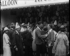 A Crowd of People Standing in Front of a Carnival Game. A Man in a Clown's Hat Encourages..., 1924. Creator: British Pathe Ltd