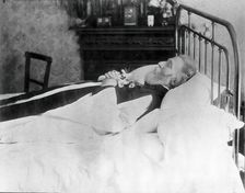 A dead man, wearing robes, lying on his deathbed, (1900?). Creator: Unknown