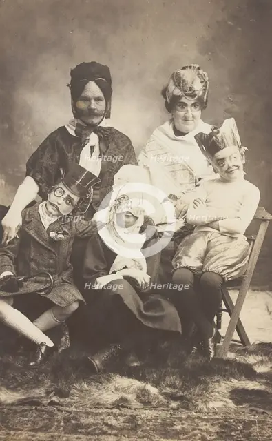 A family, all members wearing grotesque masks, the father in drag, c1910. Creator: Unknown.