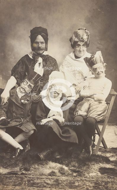 A family, all members wearing grotesque masks, the father in drag, c1910. Creator: Unknown.