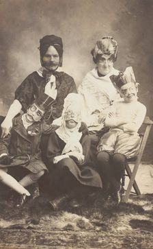 A family, all members wearing grotesque masks, the father in drag, c1910. Creator: Unknown