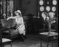 A Female Civilian Modelling a Two Piece Suit and Hat Sitting on a Sofa by a Window in a Draw... 1920 Creator: British Pathe Ltd