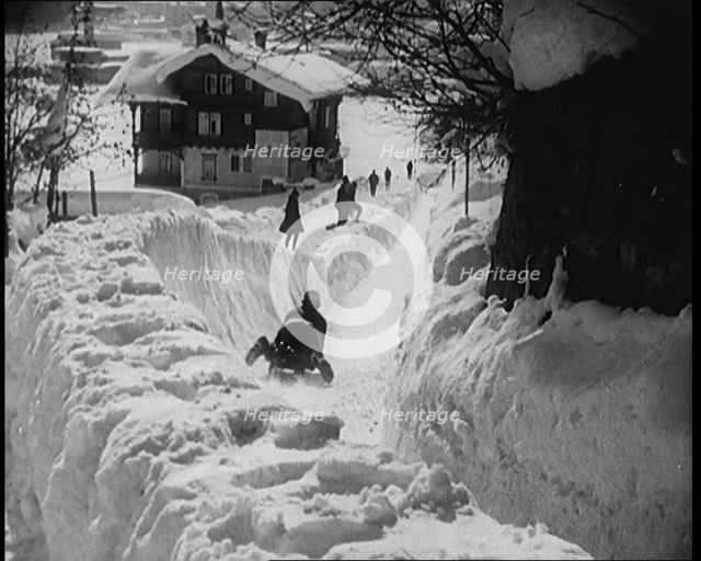 A Female Civilian Sledging down a Snowy Track Watched by Other Civilians with a Picturesque..., 1920 Creator: British Pathe Ltd.