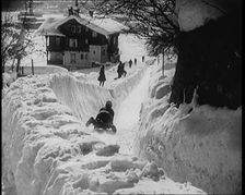 A Female Civilian Sledging down a Snowy Track Watched by Other Civilians with a Picturesque..., 1920 Creator: British Pathe Ltd