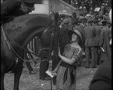 A Female Civilian Wearing a Dress and a Large Hat with a Ribbon Petting a Horse on the Nose at a Hor Creator: British Pathe Ltd