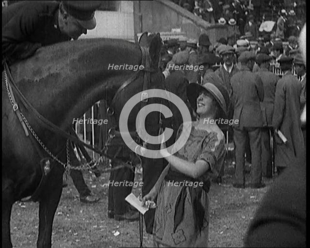 A Female Civilian Wearing a Dress and a Large Hat with a Ribbon Petting a Horse on the Nose at a Hor Creator: British Pathe Ltd.