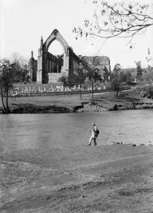 A fisherman on the River Wharfe in front of the ruins of Bolton Priory, North Yorkshire, 1940. Artist: Walter Scott