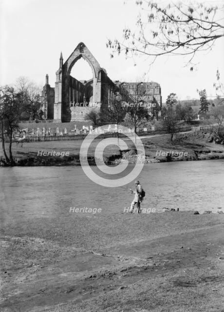A fisherman on the River Wharfe in front of the ruins of Bolton Priory, North Yorkshire, 1940. Artist: Walter Scott.