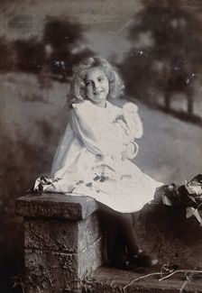 A girl, holding a doll, sitting on a wall, c1890s. Creator: Lock & Whitfield