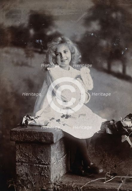 A girl, holding a doll, sitting on a wall, c1890s. Creator: Lock & Whitfield.