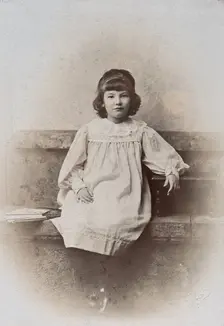 A girl, sitting on a stone bench with a fan folded at her side, c1890s. Creator: Arthur Reston