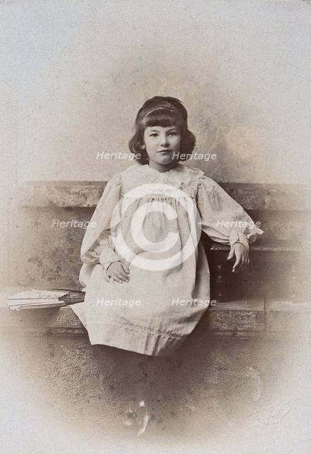 A girl, sitting on a stone bench with a fan folded at her side, c1890s. Creator: Arthur Reston.