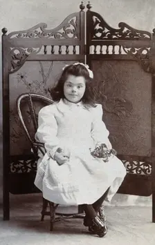 A girl with Down's syndrome, sitting in front of an ornate wooden screen..., c1870s. Creator: Charles Marshall