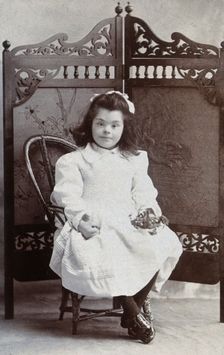 A girl with Down's syndrome, sitting in front of an ornate wooden screen..., c1870s. Creator: Charles Marshall