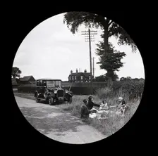 A group of women and girls having a picnic near a parked car at the side of a road..., 1920s-1930s. Creator: Norman Kingsley Harrison