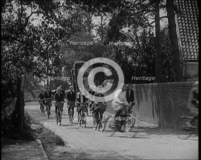 A Group of Young Female Civilians Wearing School Uniforms Riding Bicycles Along a Dusty Road, 1920. Creator: British Pathe Ltd.