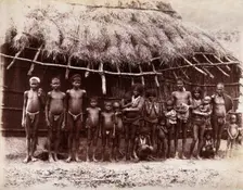 A group of adults and children standing in a line outside a bamboo hut with a thatched..., 1896/1897 Creator: Unknown